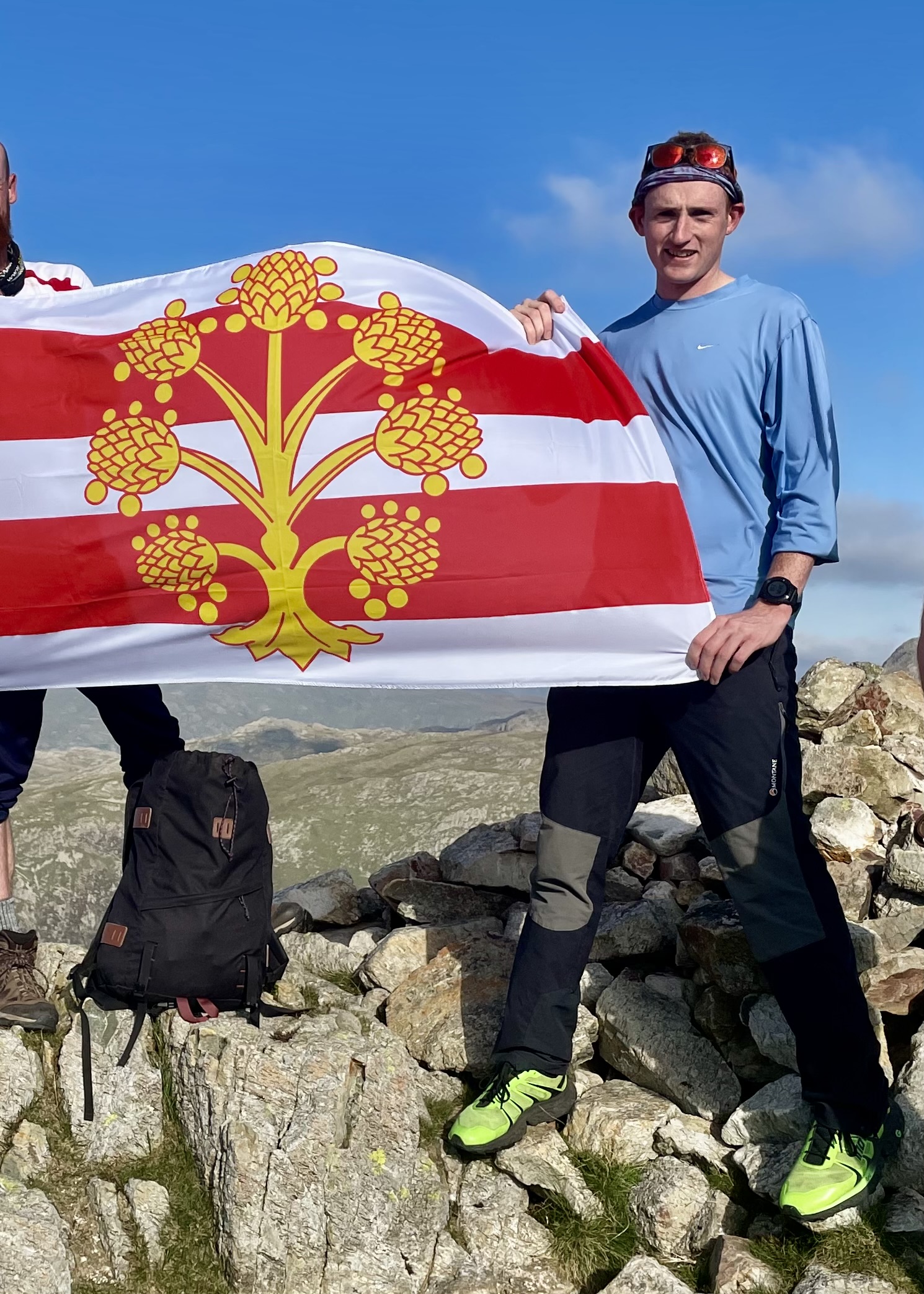 Matty Jackman stands atop Base Brown, proudly hoisting the County Flag of Westmorland, having completed all 214 Wainwright's (in 2021) II